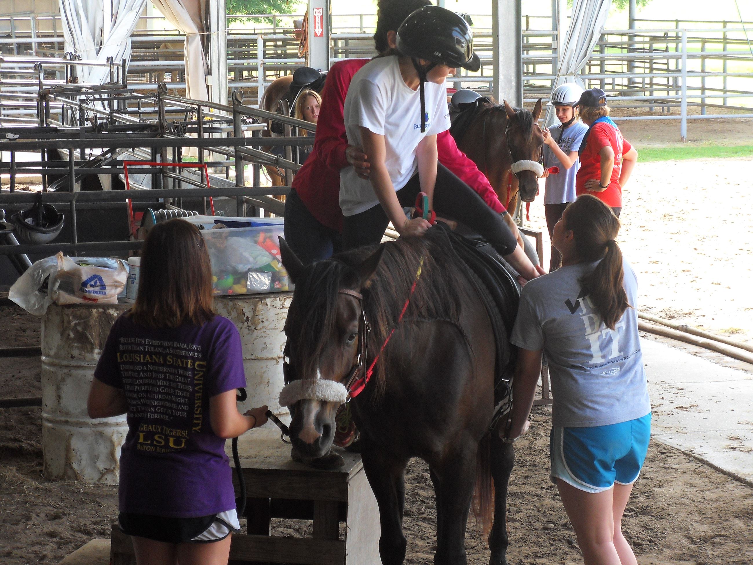 Woman assisting girl getting on horse